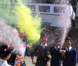 Indian children in blue and white school uniforms spray coloured powder at each other to celebrate Holi