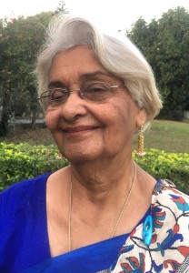 An elderly Indian woman with white hair in a sari smiles at the camera