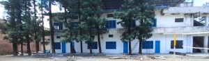 White, two story school building in India, with tall trees in front of it